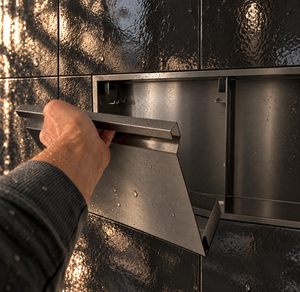 A hand lifts the removable door off the door niche, 12 × 48 in, black PVD