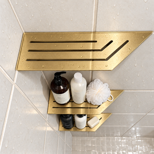 Corner shelf, 4 × 12 in, gold PVD, bottles and a shower puff on the lower shelves, in a tiled shower