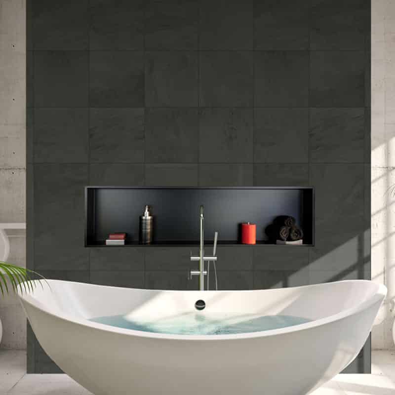 Longue niche noire garnie d’un livre, d’un flacon-pompe et d’une bougie rouge, en mur d’ardoise au-dessus d’une baignoire