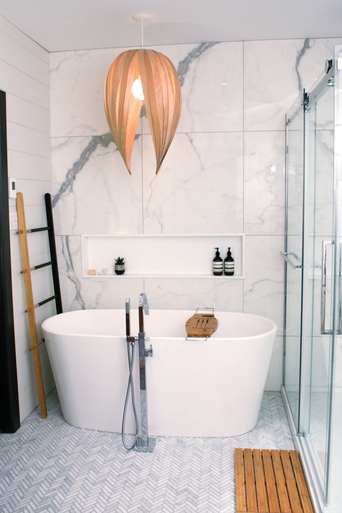 Niche Alba 12 × 48 po en blanc mat dans un mur de marbre, au fond d’une salle de bain avec baignoire autoportante et douche vitrée