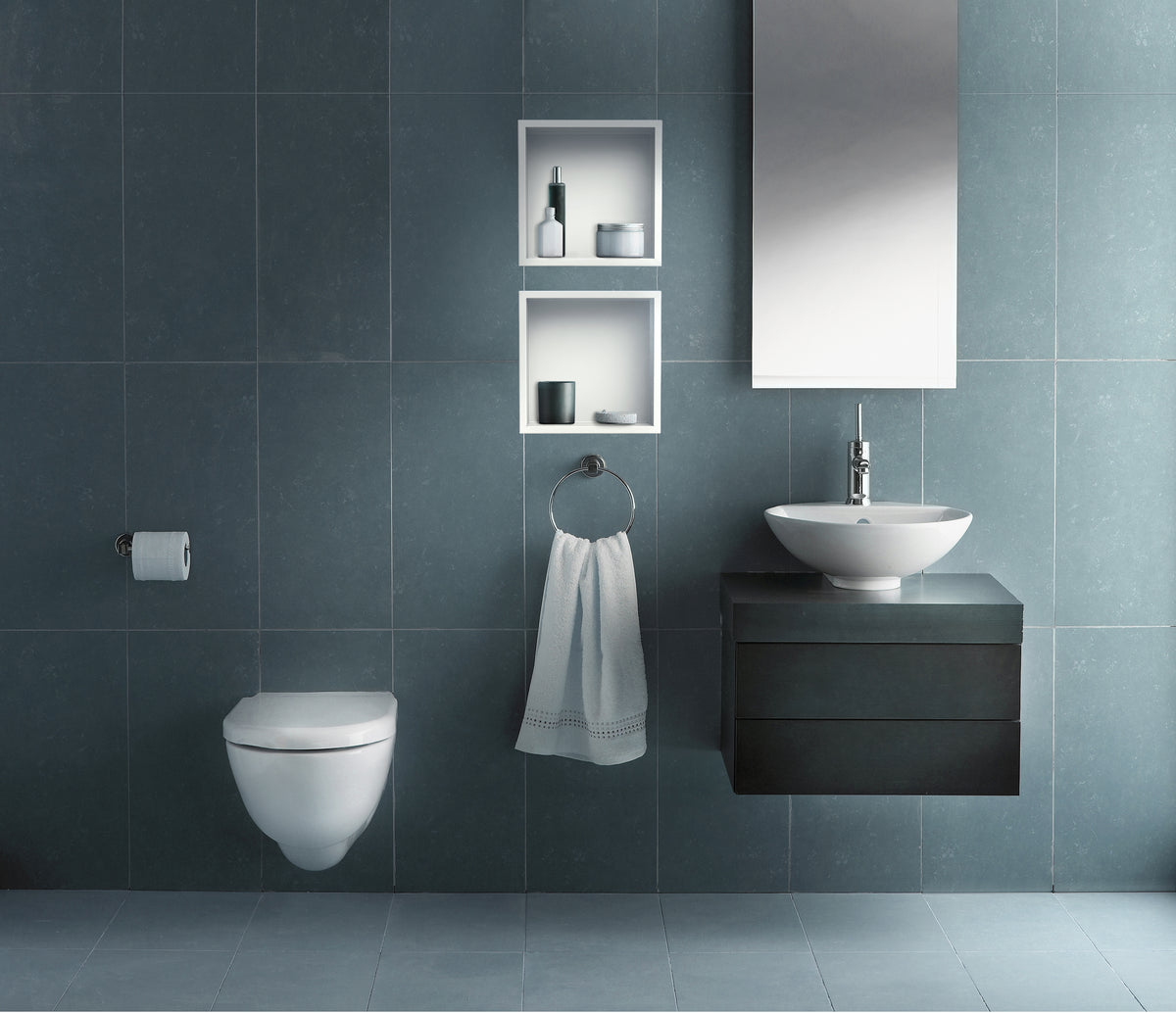 Two stacked Ally wall niches, 12 × 12 in, matte white, on a blue-gray tile wall above a wall-hung toilet and a vessel sink