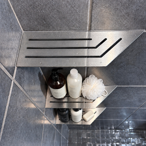Corner shelf, 4 × 12 in, brushed stainless steel, bottles and a shower puff on the lower shelves, in a tiled shower