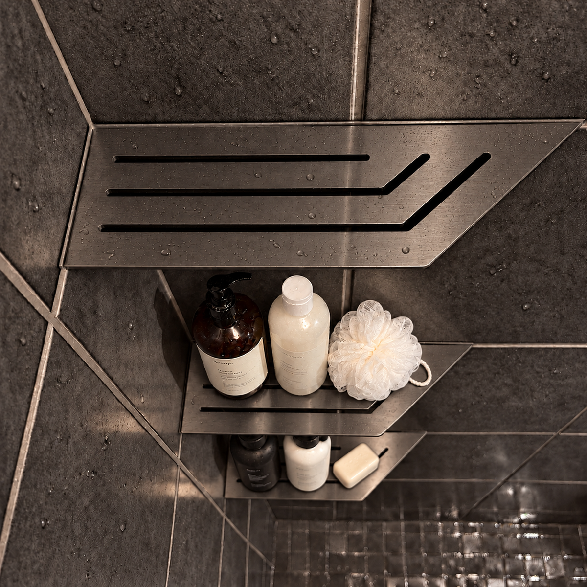 Corner shelf, 4 × 12 in, black PVD, bottles and a shower puff on the lower shelves, in a tiled shower