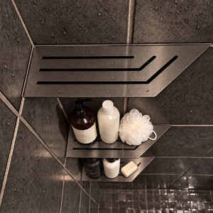 Corner shelf, 4 × 12 in, black PVD, bottles and a shower puff on the lower shelves, in a tiled shower